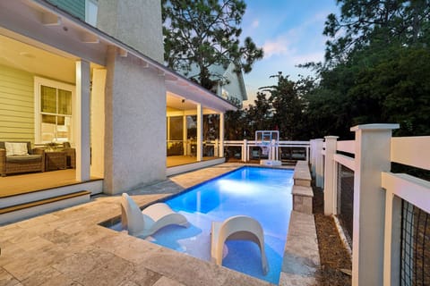 Your private pool awaits, glowing softly in the evening light, complete with poolside loungers and a basketball hoop for playful afternoons. Step out from your bright, welcoming living space onto the deck and slip into complete relaxation.
