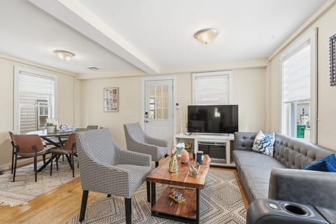 Relax and connect in the bright, open-concept living and dining area, featuring ample comfortable seating, natural light, and a large flat-screen TV.