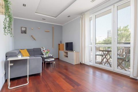A spacious living area with a gray sofa and large balcony windows. The room is filled with natural light and has a modern design.