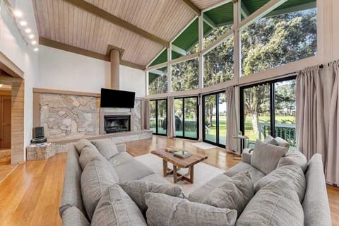 Deep sectional seating faces stone fireplace beneath dramatic garden windows