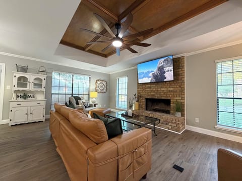 Bright living room with brick fireplace, TV, and stunning wood tray ceiling