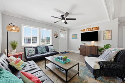 Relax in your bright, beach-themed living room with comfy seating, ceiling fan, and flat-screen TV—perfect for unwinding after a day of coastal adventures.