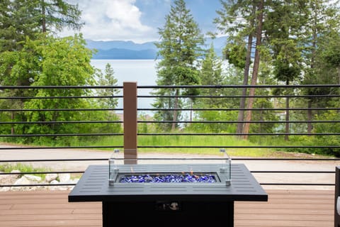 Stunning lakefront deck features a modern fire table overlooking tranquil waters and mountain peaks—perfect for unwinding after exploring.