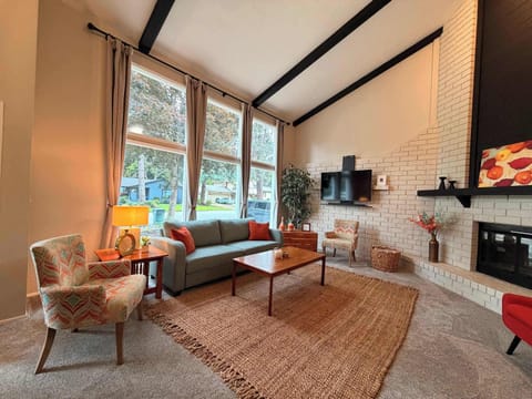Bright living room with vaulted beamed ceiling, large picture windows, and white brick accent wall — warm mid-century charm from the moment you walk in