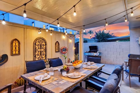 Covered patio dining area with string lights, BBQ grill, and a relaxed sunset setting.