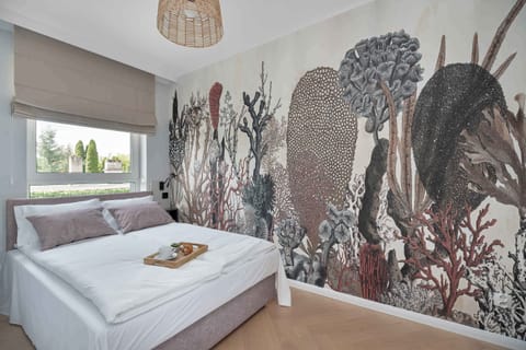 Bright bedroom featuring a comfortable double bed, artistic feature wall, and large window with natural daylight.