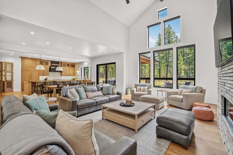 Settle into this stunning open-concept living space where soaring ceilings and floor-to-ceiling windows frame peaceful forest views. The inviting seating area flows seamlessly into a warm kitchen and dining space—perfect for gathering and unwinding.