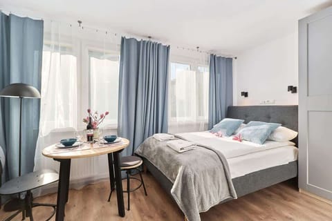 A cozy bedroom featuring double bed with white and blue linens, bedside tables, and large windows letting in natural light.
