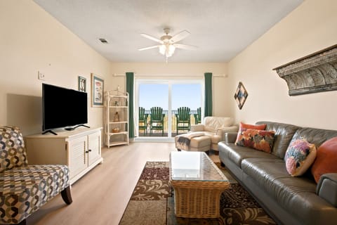 Unwind in your cozy living space with comfortable seating, a large TV for movie nights, and a private balcony with inviting beach chairs overlooking the water.