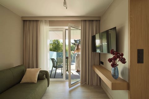 Salon został urządzony w nowoczesnym stylu, łączącym naturalne drewno, jasne beże i oliwkową zieleń. Znajduje się w nim wygodna, rozkładana sofa. Z pomieszczenia można wyjść bezpośrednio na balkon.