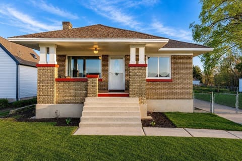 Brick exterior house with covered front porch, white door, and concrete steps leading to a green lawn.
