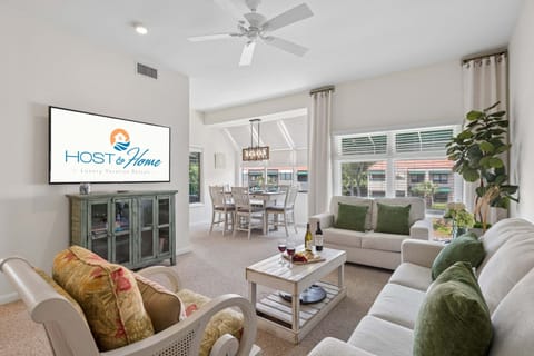 The living room offers a relaxed, coastal-cottage feel with soft neutral tones, a mix of cozy seating, and plenty of natural light pouring in through tall windows.