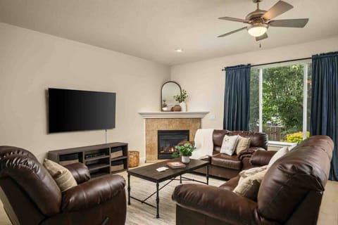 An inviting living room featuring plush leather seating, a corner gas fireplace, and seamless flow into the adjacent dining area and kitchen.