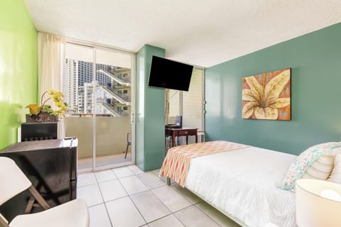 A vibrant bedroom blending green and teal walls with colorful artwork. Your private balcony opens to city views, while a flat-screen TV and fresh linens ensure comfort throughout your stay.