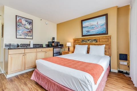Your cozy island escape awaits, with a plush bed beneath vibrant tropical artwork and a convenient kitchenette for morning coffee—everything you need to unwind in style.