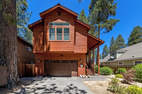 Charming mountain cabin with warm cedar siding and a two-car garage nestled among towering pines in a peaceful, tree-lined neighborhood.