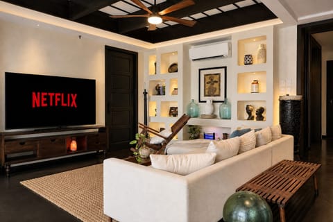 【Living Room】Centered around an L-shaped sofa and a 65‑inch smart TV with Netflix and other streaming services. Supported by 500 Mbps Wi‑Fi, it’s ideal for smooth streaming. The room also features built‑in shelves with books and antique pieces.