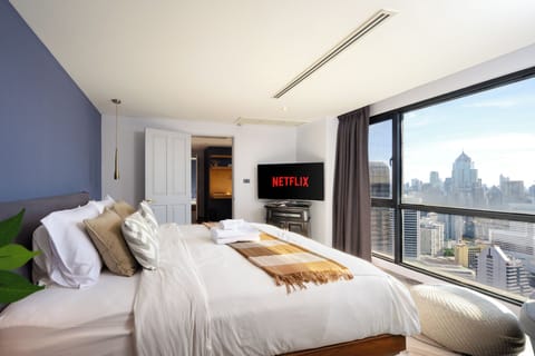 【Master Bedroom with a View】The king bed faces the open Bangkok skyline so the city is the first thing you see at sunrise and the last before sleep. Blackout curtains, dedicated AC, and Netflix already signed in for the stay.