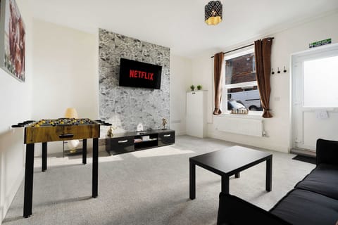Upon entry, you'll find a comfortable living room with a sofa bed, coffee table, side tables, and a Smart TV. Wi-Fi details, a retro gaming console, books, and card games are provided. The fuse board and electric meter are also located here.