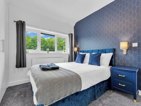 Bright, stylish bedroom with plush blue accents and peaceful leafy views