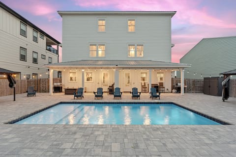 Resort-style backyard with private pool, covered game lounge, hot tub, and sunset skies.
