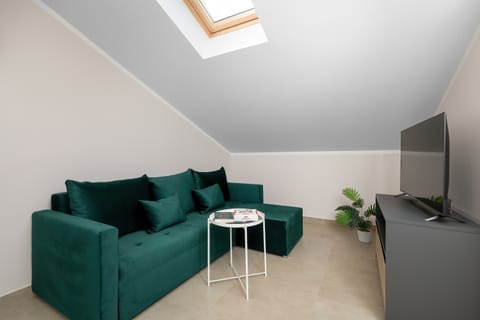 Stylish attic studio featuring a comfortable velvet sofa, Smart TV and cozy lounge area beneath exposed wooden beams.