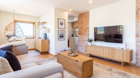 Relax in the bright and inviting living area, featuring a comfortable sofa and a unique hanging chair where you can unwind, with exposed brick adding character and an open flow to the modern kitchen. This space is designed for both lively conversations an