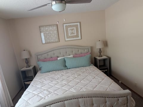 Bedroom with tufted beige headboard, quilted bedding in white and teal, flanked by gray bedside tables and lamps.