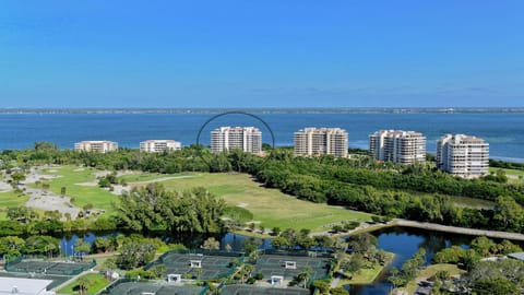Aerial view highlighting the condo building surrounded by tennis courts, golf course greenery, and bay waters.