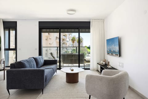Contemporary living room merges sleek dark sofa with warm neutral accents and natural light from expansive windows.
