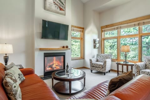Settle into this bright living room with crackling fireplace, plush seating, and floor-to-ceiling windows framing peaceful forest views—your perfect retreat after a day of adventure.