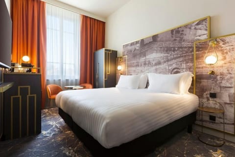 A classic room with a plush king-size bed, warm stone-effect feature wall, and rich terracotta curtains — elegant comfort in the heart of Nîmes.