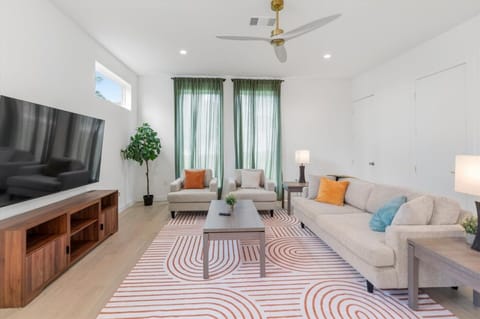 Sink into the oversized sectional and matching accent chairs for movie nights or slow mornings. A sculptural brass fan, soft green drapes, and warm wood floors set the mood, with playful pops of citrus and teal. The room where memories are made.