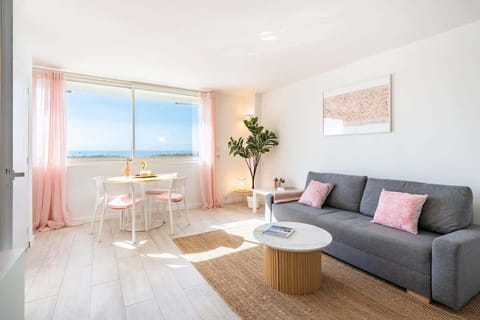 Le matin, la lumière traverse les rideaux roses et illumine la table ronde face à la mer; installez-vous sur le canapé gris avec un livre et savourez ce coin cosy et apaisant.