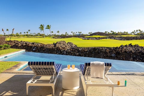 Ease into the day from a private lounger overlooking the infinity pool, lava rock landscape, and rolling fairway beyond.