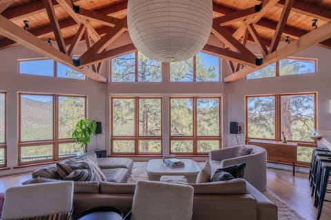 Relax in this stunning living room where soaring ceilings and floor-to-ceiling windows frame breathtaking mountain and forest views, creating your perfect mountain retreat.