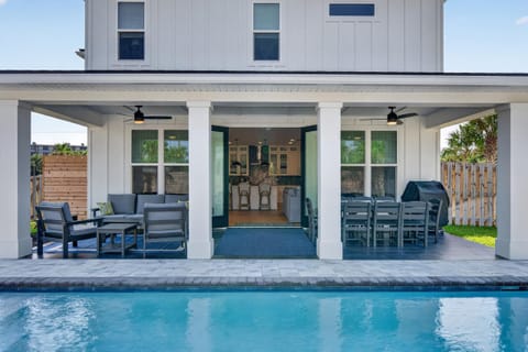 Covered patio with gray wood seating and dining sets overlooks a heated saltwater pool with tiled deck.