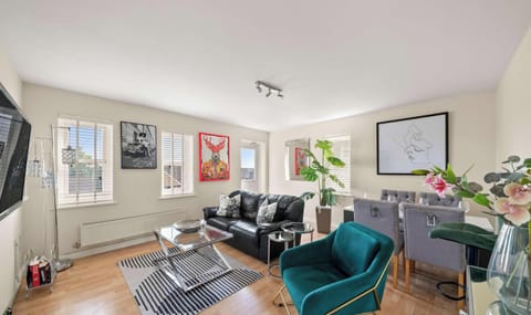 This bright, living and dining room features a black leather sofa, a teal armchair, and a glass coffee table over a striped rug.