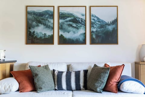 Unwind on this plush white sofa, styled with colorful throw pillows and framed by a serene three-panel mountain wall art triptych.