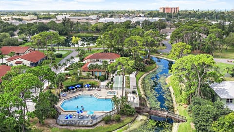 Aerial view of a vacation resort featuring an outdoor pool, tree-lined canal, and residential buildings set within a lush tropical landscape.