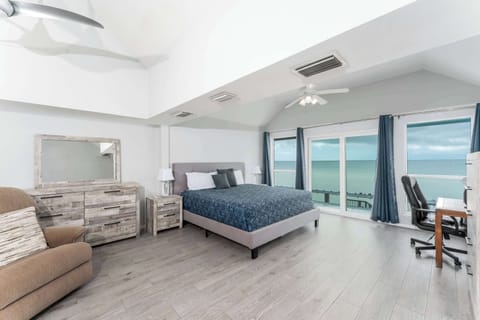 Primary Bedroom with King Bed & Ensuite — Spacious upstairs retreat with king bed, TV, and floor-to-ceiling water views. Ensuite bathroom includes shower and vanity.