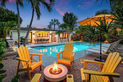 Heated pool and gas fire pit lit at dusk, with Adirondack seating for six.