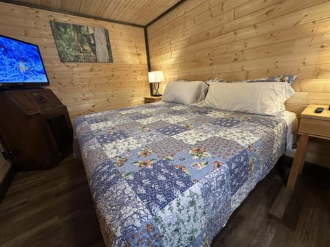Bedroom with wood-paneled walls, a patchwork quilt on the bed, a bedside lamp, and a wall-mounted TV.