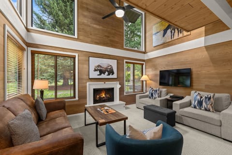 Sunlit great room with fireplace, tall windows, and cozy modern-rustic style