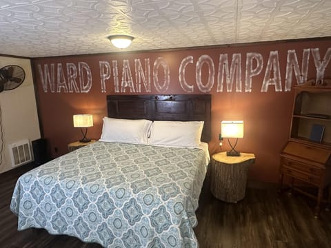 Bedroom with dark wood headboard, patterned blue-gray bedspread, rustic log nightstands, and vintage secretary desk.