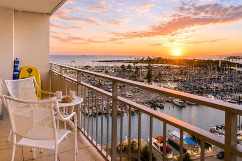 Golden-hour on your private lanai - sailboats dotting Ala Wai Harbor, the Pacific glowing amber, and a bistro table set for two. The signature Ilikai sunset, nine floors up.