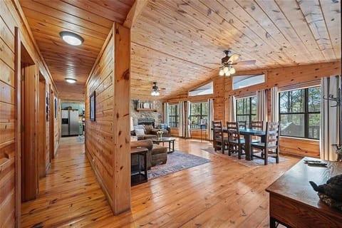 Picture yourself relaxing in this warm, wood-paneled cabin with vaulted ceilings, comfortable seating, and a stone fireplace. Large windows frame your peaceful forest escape perfectly.