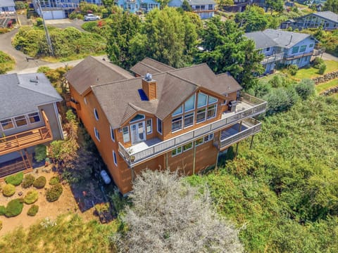 Aerial view of a spacious multi-level vacation rental home with expansive deck and lush landscaping in a quiet coastal neighborhood.