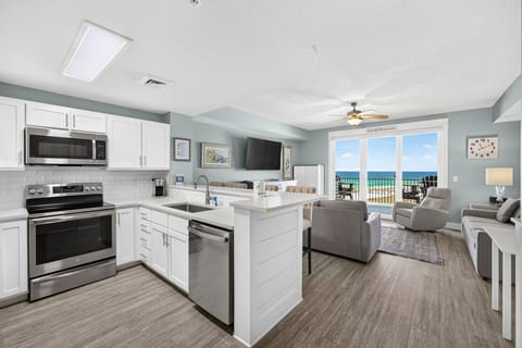 Step into an open, light-filled space where your kitchen flows effortlessly into a cozy living area. Crisp white cabinetry and modern appliances make meal prep a breeze while you enjoy stunning ocean views through expansive glass doors.