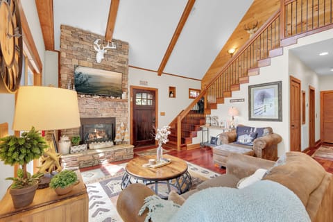 Gather beneath soaring wood beams in a lodge-style living room built for mountain memories—flames dancing in the stone fireplace, rustic charm all around, and the perfect spot to unwind after a day on the slopes.
